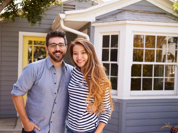 A woman and a man in their thirties smiling in front of their ADU.