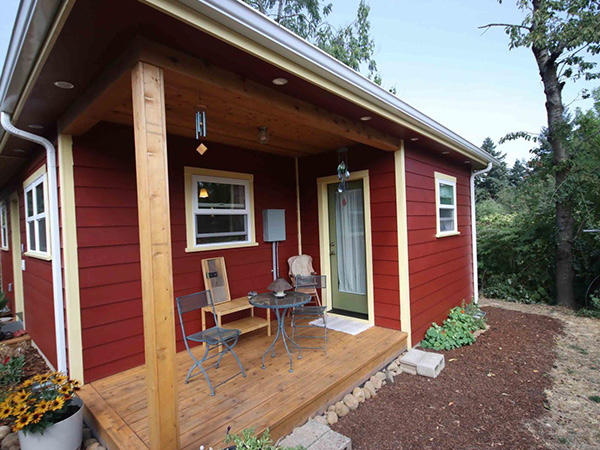 Red ADU with small covered porch with chairs and a table.