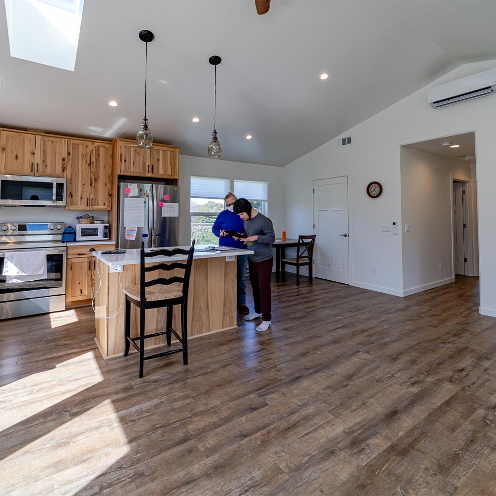Gabe, Joni and Scott’s adult son, stands with a caretaker by the island in the kitchen. Pitched ceiling and abundant natural light make space feel very big.