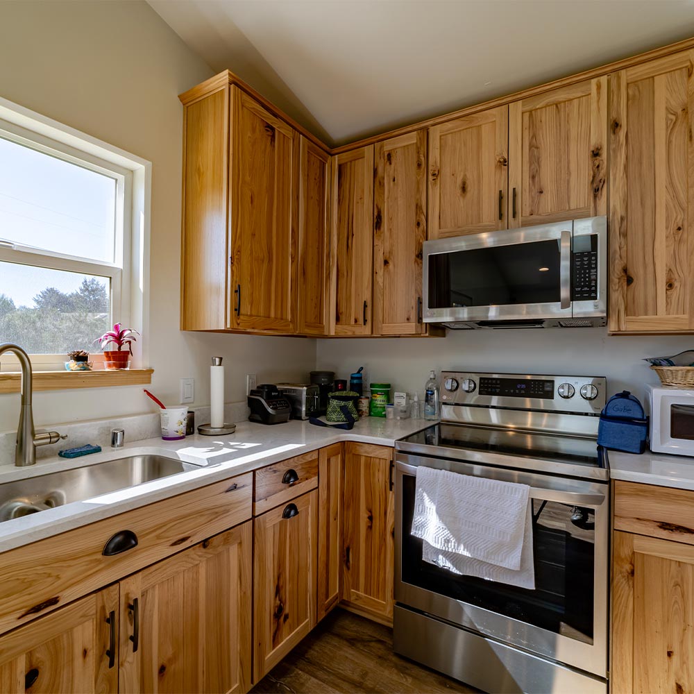Large basin sink, oven, microwave with wooden cabinets and sun-dappled countertop.