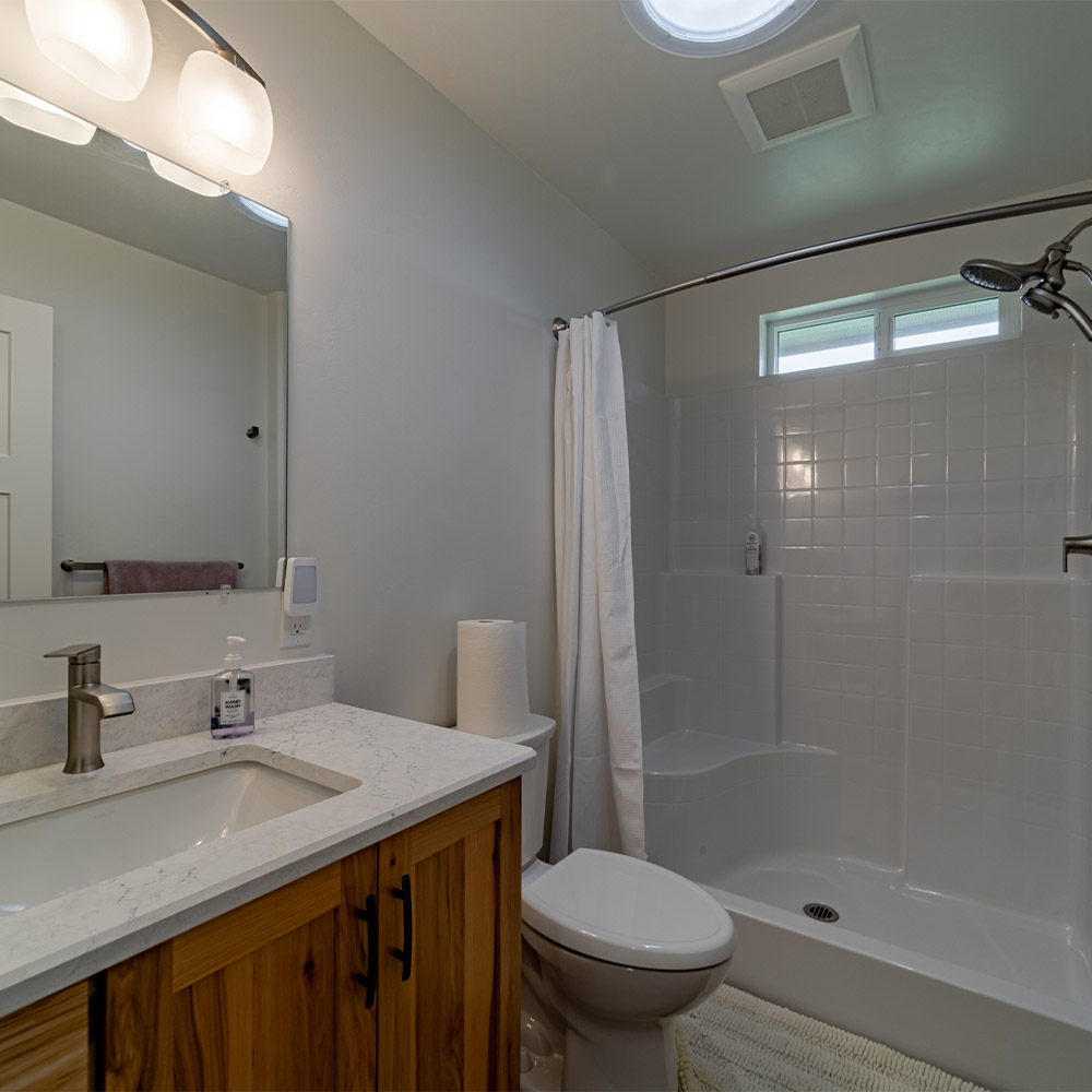 Bathroom with large shower equipped with multiple nozzles and seat. Sink, clean counter and toilet in foreground.