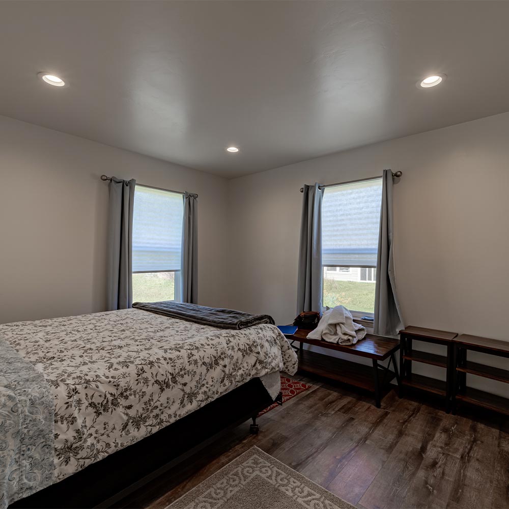 Interior of bedroom with floral bedspread, two windows and wooden shelving.