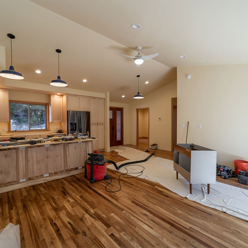 Kitchen with modern fridge, with island under construction, shop vac and various tools on the floor on the interior of ADU.