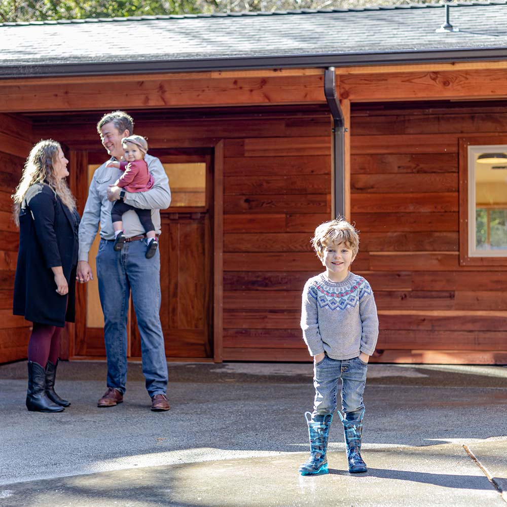 A child stands in front of a woman and a man holding a baby. The entrance to an ADU is in the background.