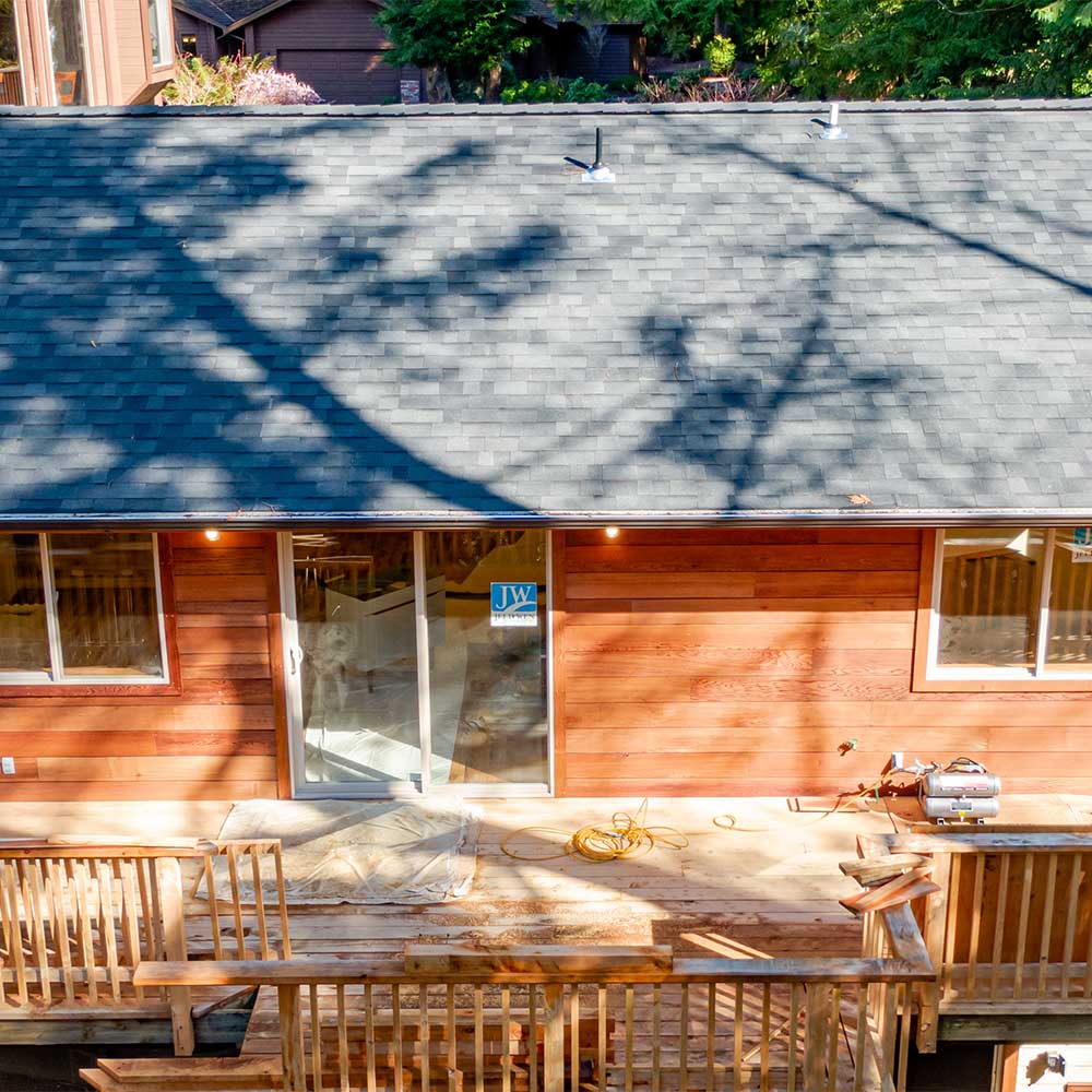 Dappled sunlight on an ADU with wooden siding, new glass door and deck that is under construction.